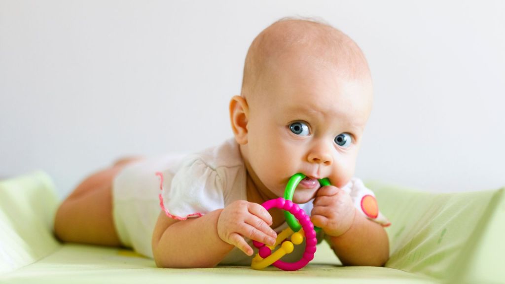 Baby chewing on teething toy on a green changing table.